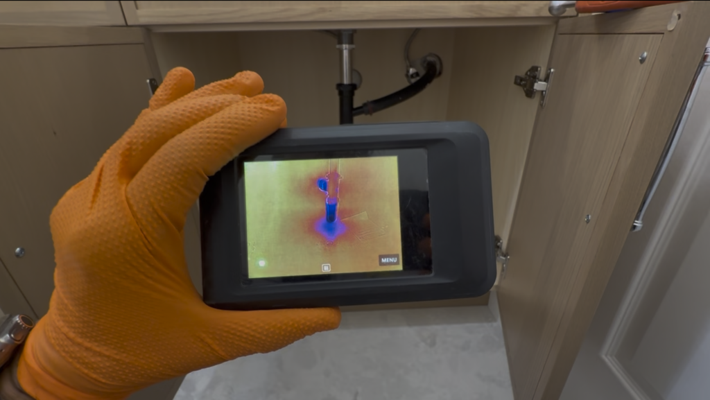 Home inspector using a thermal camera to examine plumbing beneath a sink